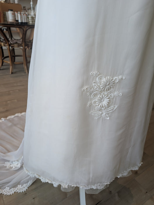 Pine Eco + Refillery Boutique white wedding gown featuring intricate floral lace appliqué on a flowing fabric skirt.